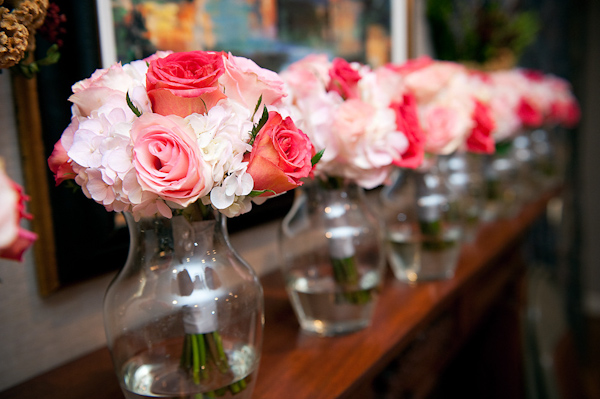 bridesmaids' bouquets of dark pink, light pink, coral, and ivory flowers in clear vases sitting in a row on top of fireplace mantle -photo by Houston based wedding photographer Adam Nyholt